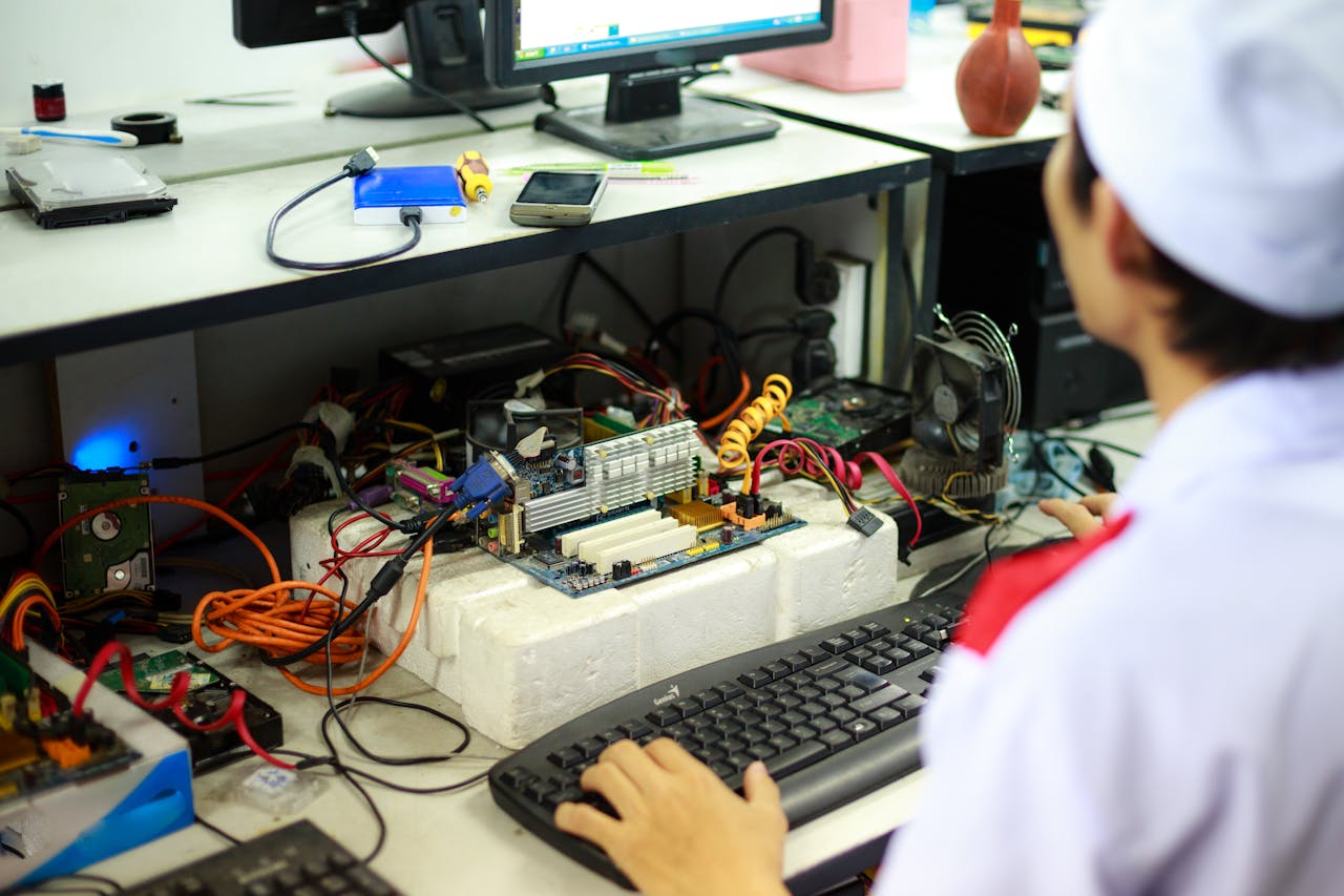 About A man in a laboratory uniform working on computer components and wiring at a workstation.