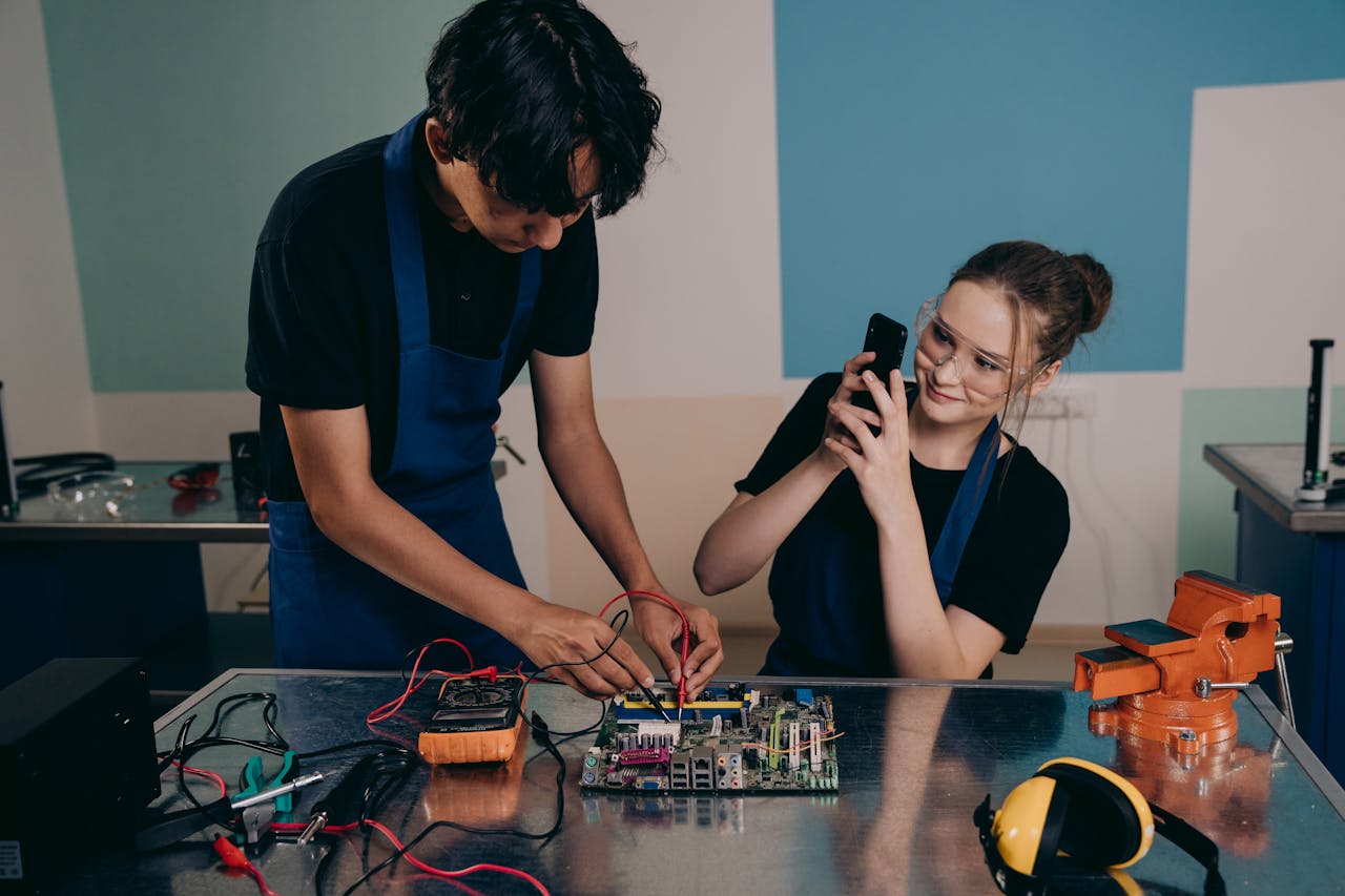 Services Two young adults testing a motherboard in a tech lab, capturing the process with a smartphone.